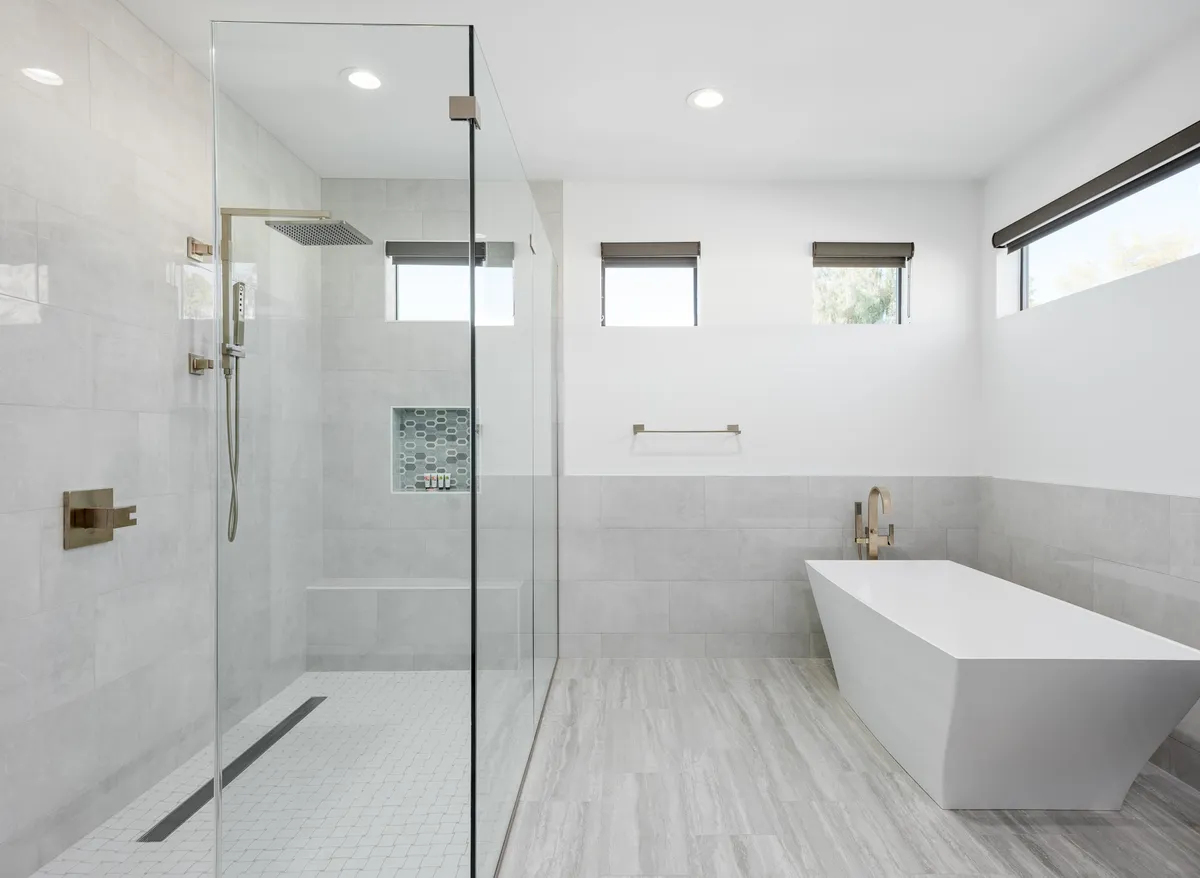 A spa-inspired bathroom with a glass shower enclosure, a freestanding soaking bathtub, textured wall tiles, and ample natural light. The design conveys a sense of luxury and relaxation.