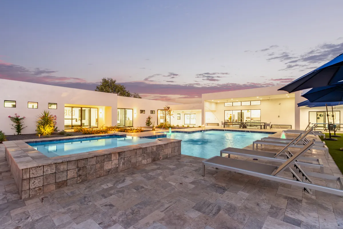 An elegant exterior view showcases a luxurious swimming pool and an adjoining hot tub, complemented by plush lounge chairs and beautifully landscaped gardens. The calm setting is ideal for relaxed socializing, morning coffee, or hosting a poolside gathering.