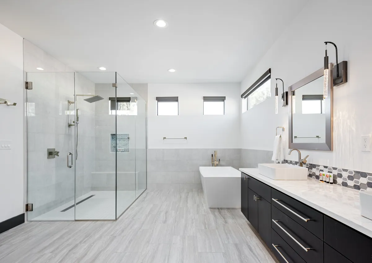 A luxurious bathroom with a glass shower enclosure, freestanding bathtub, and an elegant vanity with a large mirror. The design is tranquil and spa-like, offering an indulgent experience for guests.
