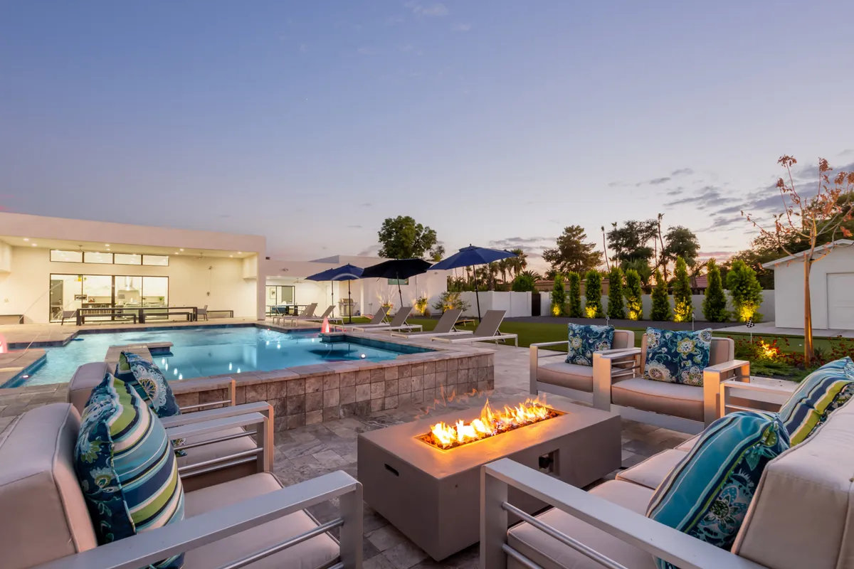 This exterior shot features a sparkling pool surrounded by lounge chairs and umbrellas, with a fire pit area nearby. The setting is lush and inviting, ideal for group gatherings and downtime in the evening after productive work sessions. The image captures both the pool and socializing areas, evoking relaxation and team bonding.