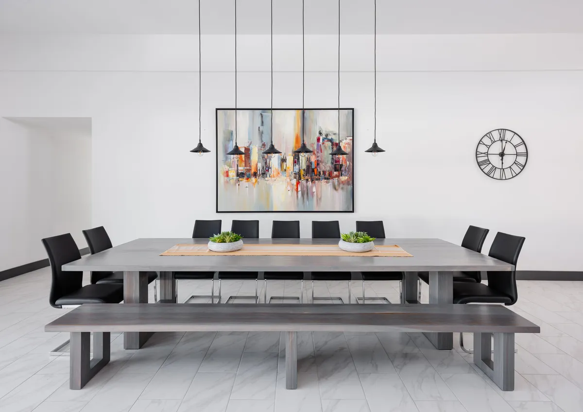 A formal, elegant dining room with a large, modern dining table surrounded by black chairs, striking pendant lights above, and contemporary artwork adorning the wall. The setting exudes an air of sophistication and is designed for memorable gatherings and special occasions.