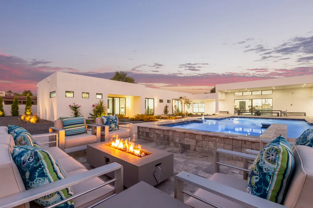 A cozy fire pit area adjacent to the swimming pool, surrounded by outdoor seating and modern landscaping. The warm lighting and tranquil mood evoke evenings spent stargazing and sharing stories by the fire.