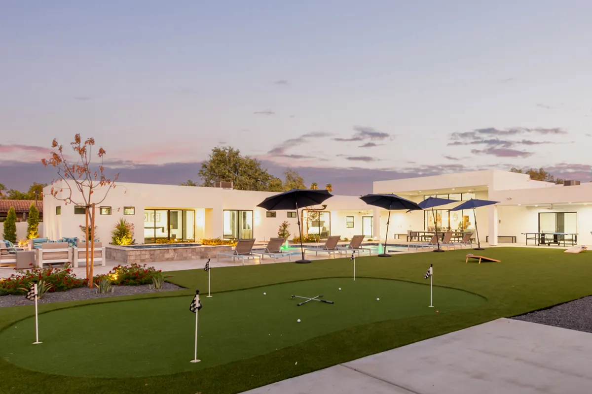 A vibrant outdoor scene with a putting green in the foreground, a sparkling swimming pool, shaded seating area, and umbrellas. The image conveys a playful yet leisurely atmosphere, ideal for both golf enthusiasts and families.
