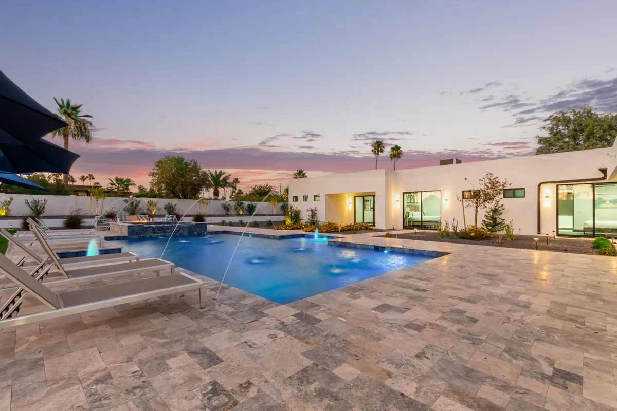 A resort-style swimming pool surrounded by lounge chairs, elegant fountains, and palm trees, all bathed in soft evening light. The space looks inviting for both daytime leisure and nighttime festivities.