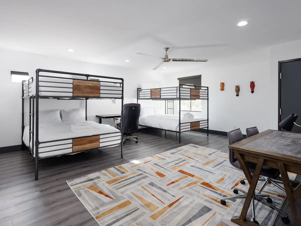 A chic bunk room designed with built-in bunk beds, a modern workspace, decorative masks, and a cozy area rug. The room is playful yet sophisticated, catering to younger guests or groups seeking a fun retreat.