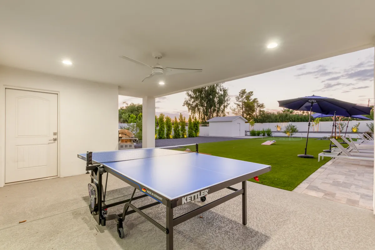 This image captures a lively games area with a ping pong table, outdoor seating, and an umbrella on a bright green lawn. The space encourages friendly competition and group activities, surrounded by comfortable gathering spots.